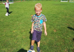 Szymon ze "Skrzatów" z piłką na boisku sportowym.