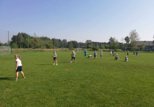 "Skrzaty" biorą udział w zabawie ruchowej na boisku sportowym.