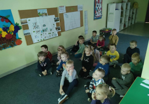 Dzieci z grupy "Pszczółek" oglądają film edukacyjny pt. "Skąd się biorą produkty ekologiczne?" na tablicy interaktywnej.