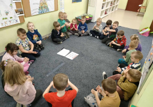 Dzieci z grupy "Pszczółek" siedzą w kręgu na dywanie i wraz z nauczycielką ćwiczą technikę prawidłowego mycia rąk.