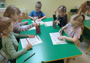 Kilkoro dzieci przy stoliku starannie koloruje wszystkie produkty oraz aktywności na szablonie piramidy zdrowego żywienia.
