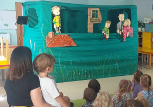 Dzieci oglądają przedstawienie. Przed nimi stoi scena, na której rozgrywa się akcja spektaklu.