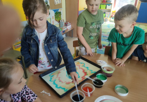 Dzieci z "Wiewiórek" tworzą swój wspólny obraz malowany na mleku.