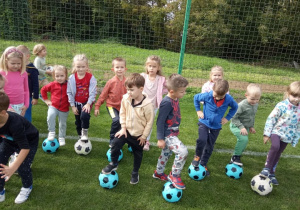 Kilkoro dzieci z grup "Biedronki" oraz "Kaczuszki" na boisku z piłkami.