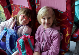 dwie dziewczynki z grupy "Skrzaty" uśmiechają się podczas podróży autokarem