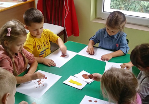 Kilkoro dzieci z grupy "Biedronek" przy stoliku podczas malowania kasztanem.