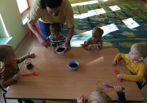 Kilkoro dzieci z grupy "Motylków" wraz z ciocią Krzysią przy stoliku podczas tworzenia "jadalnego lasu w słoiku".