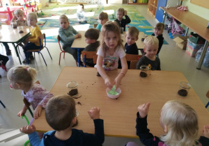 Kilkoro dzieci z grupy "Motylków" przy stoliku podczas tworzenia "jadalnego lasu w słoiku".