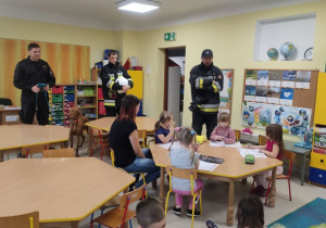 Kilkoro dzieci z grupy "Skrzatów" wraz z ciocią Martą podczas pogadanki o zachowaniu w sytuacji nagłego zagrożenia, prowadzonej przez strażaków.