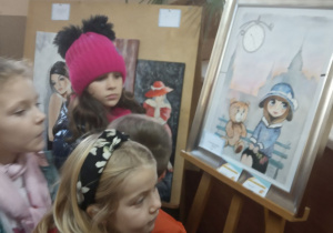 Kilkoro dzieci ogląda pracę malarską ozorkowskiej artystki Danuty Michałowskiej.
