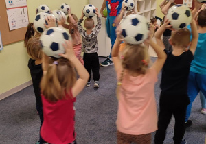 Dzieci z grupy "Biedronek" trzymają piłki nad głową.