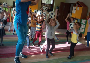 Dzieci z grupy "Kaczuszek" trzymają piłki nad głową.