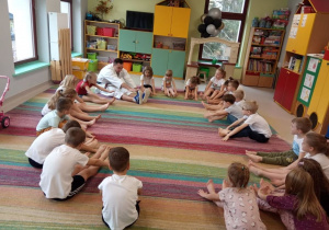 Dzieci z grupy "Kaczuszek" wraz z trenerem karate podczas ćwiczenia rozciągającego.