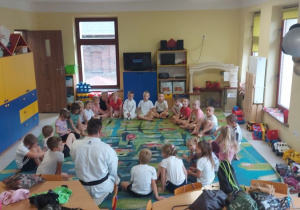 Dzieci z grupy "Skrzatów" siedzą na dywanie i uważnie słuchają trenera.