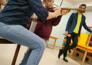 Chłopiec ze starszej grupy podczas gry na skrzypcach przy wsparciu pani prowadzącej.