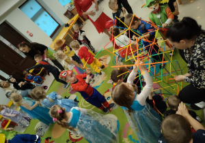 Dzieci wspólnymi siłami wraz z ciocią Krzysią tworzą ogromną konstrukcję z kolorowych patyczków i łączników.