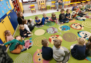 Dzieci siedzą na dywanie i uważnie obserwują.