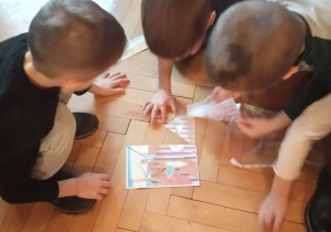 Troje przedszkolaków układa puzzle ilustrujące dzieło malarskie.