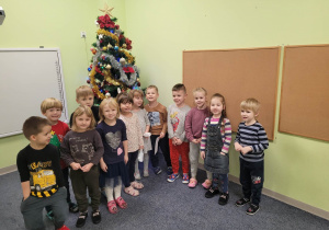Dzieci z grupy "Biedronek" podczas zabaw mikołajkowych pozują do zdjęcia. Za dziećmi stoi pięknie ubrana choinka.