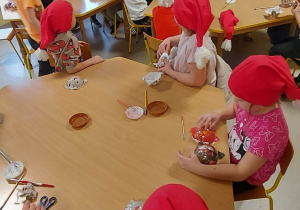 Dzieci z grupy "Skrzatów" przy stołach podczas słuchania instrukcji, jak ozdobić bombkę.