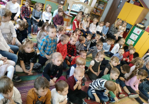 Dzieci z naszego przedszkola siedzą na dywanie i uważnie słuchają Księdza.