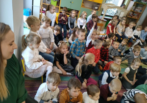 Dzieci z naszego przedszkola siedzą na dywanie i uważnie słuchają Księdza.