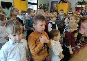 Przedszkolaki stoją i słuchają fragmentu Pisma Świętego.