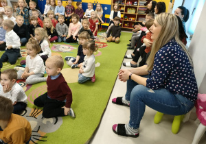 Przedszkolaki siedzą na dywanie i uważnie słuchają podczas audycji muzycznej.