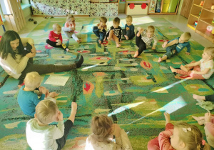 Dzieci z grupy "Motylków" wraz z ciocią Agnieszką na dywanie podczas zabawy w telefon.