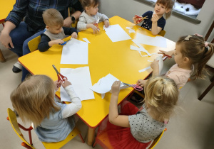 Kilkoro dzieci z grupy "Motylków" przy stole rozcina białą kartkę na małe kawałeczki.