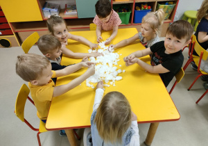 Kilkoro dzieci z grup młodszych przy stoliku podczas określania właściwości przygotowanego sztucznego śniegu.