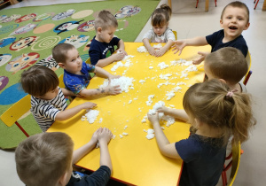 Kilkoro dzieci z grup młodszych przy stoliku podczas zabawy sztucznym śniegiem.