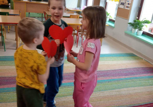 Troje dzieci z grupy Kaczuszek na dywanie podczas zabawy do piosenki "Serduszko przyjaźni".