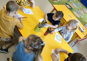 Kilkoro dzieci z grupy "Pszczółek" przy stoliku koloruje szablon pączka.