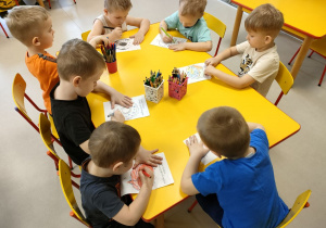 Kilkoro dzieci z grupy "Pszczółek" przy stoliku koloruje szablon pączka.
