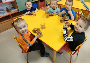 Kilkoro dzieci z grupy "Pszczółek" przy stoliku podczas podwieczorku - pączka z marmoladą.
