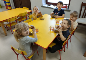 Kilkoro dzieci z grupy "Pszczółek" przy stoliku podczas podwieczorku - pączka z marmoladą.