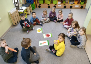 Dzieci z grupy "Biedronek" siedzą w kole na dywanie podczas pogadanki na temat roli owoców i warzyw w życiu człowieka w oparciu o artykuły i ilustracje.