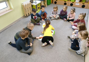 Dzieci z grupy "Biedronek" siedzą w kole na dywanie podczas pogadanki na temat roli owoców i warzyw w życiu człowieka w oparciu o artykuły i ilustracje.