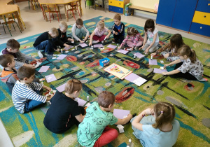 Dzieci z grupy "Skrzatów" siedzą na dywanie w trakcie składania obrazków warzyw/owoców w całość w jak najszybszym tempie.