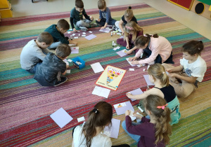 Dzieci z grupy "Kaczuszek" siedzą na dywanie w trakcie składania obrazków warzyw/owoców w całość w jak najszybszym tempie.