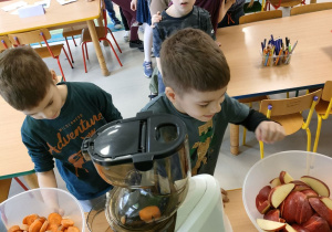 Dzieci z grupy "Kaczuszek" ustawione w "pociąg" wspólnie przygotowują naturalny sok jabłkowo-marchewkowy z dodatkiem cytryny przy wykorzystaniu sokowirówki.