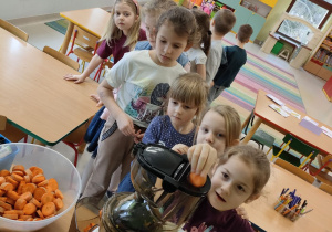Dzieci z grupy "Kaczuszek" ustawione w "pociąg" wspólnie przygotowują naturalny sok jabłkowo-marchewkowy z dodatkiem cytryny przy wykorzystaniu sokowirówki.