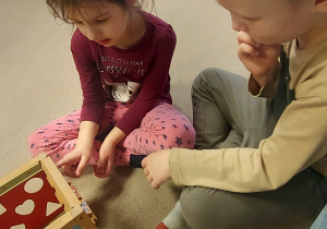 Chłopiec z dziewczynką grają w kółko i krzyżyk na manipulacyjnej drewnianej kostce.