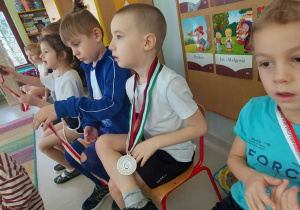 Kilkoro starszych dzieci na krzesełkach w medalach.