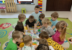 Dzieci wspólnie kolorują wiosenną kolorowankę na dużym formacie.