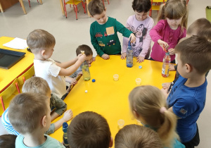 Dzieci z grupy "Pszczółek" podczas eksperymentu z wodą i barwnikami. Artur, Kajtek, Karolina i Kornel dodają do butelek z wodą farby w podstawowych kolorach.