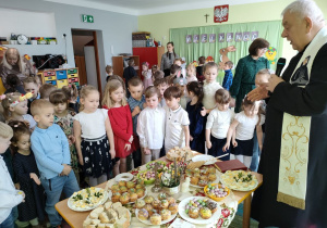 Ksiądz prezentuje dzieciom symboliczny stół wielkanocny, na którym nie może zabraknąć jajek i chleba oraz soli i pieprzu.