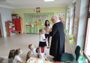 Ninka w imieniu wszystkich dzieci oraz pracowników przedszkola wręcza Księdzu upominek w ramach podziękowania za spotkanie.