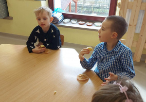 Dwóch chłopców z grupy "Skrzatów" przy stoliku podczas poczęstunku w ramach wielkanocnego spotkania z Księdzem. Dzieci otrzymały przygotowane i udekorowane przez siebie babeczki oraz słodkie, czekoladowe jajka.